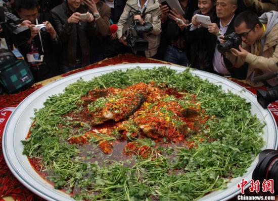 10月19日，第二十三届中国厨师节在湖南长沙举行。中国湘菜大师许菊云率团队将一条长1.4米、重102斤的罕见有机鳙鱼(雄鱼，单鱼头约重50斤)现场宰杀，烹制成“双色双味剁椒鱼头”，并申创吉尼斯纪录。图为超级剁椒鱼头引围观。唐小晴 摄